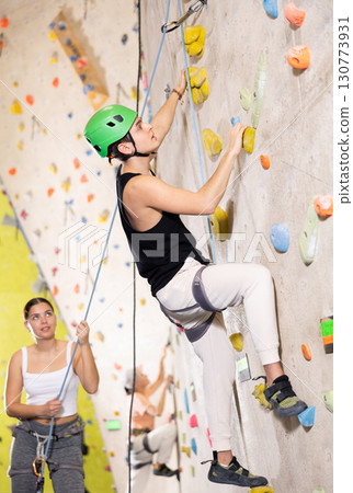 young positive man, insured by trainer, moving up artificial climbing wall indoors young positive man, insured by trainer, moving up artificial climbing wall indoors 130773931