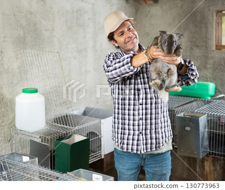 Man farmer with rabbit in her hands on her farm. Farmer takes care of animals Man farmer with rabbit in her hands on her farm. Farmer takes care of animals 130773963