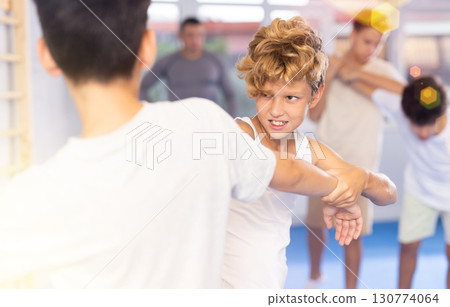 Focused kids in pair exercising self-defense movements during group class in sports studio, closeup Focused kids in pair exercising self-defense movements during group class in sports studio, closeup 130774064