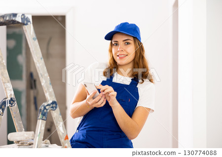 Female construction worker using smartphone in apartment 130774088