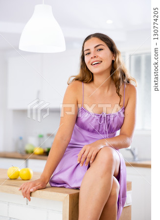 Portrait of attractive young woman sitting on kitchen table 130774205