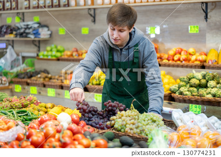 Young male seller putting pomegranates in market basket in grocery store Young male seller putting pomegranates in market basket in grocery store 130774231