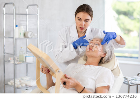 Mature patient with mirror, doctor with gloves Mature patient with mirror, doctor with gloves 130774236