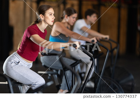 Focused girl works out with airbike during class at fitness club Focused girl works out with airbike during class at fitness club 130774337