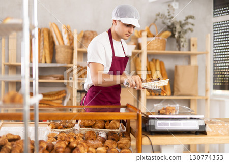 Young baker weighs fresh croissants on a scale and places them in plastic container Young baker weighs fresh croissants on a scale and places them in plastic container 130774353