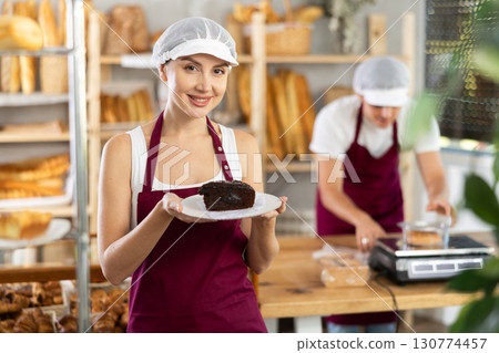 Young saleswoman holding piece of pastry in paper plate Young saleswoman holding piece of pastry in paper plate 130774457