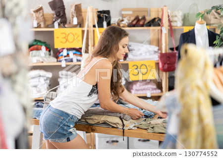 Positive young woman choosing pantaloons in clothing store 130774552