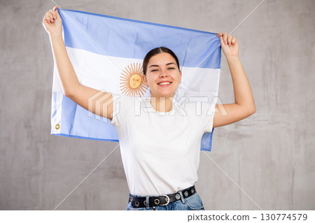 Joyous young woman holding Argentina flag against unicoloured background 130774579