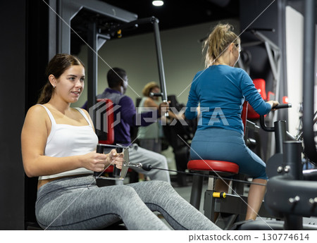 Woman is engaged in a simulator with horizontal weights in gym 130774614