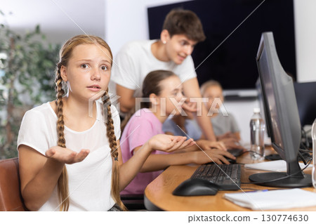 Confused preteen girl sitting at computer table in training room 130774630