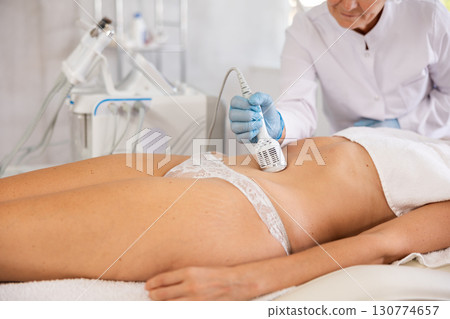 Cosmetologist performing cryotherapy using cooling attachment on female client belly 130774657