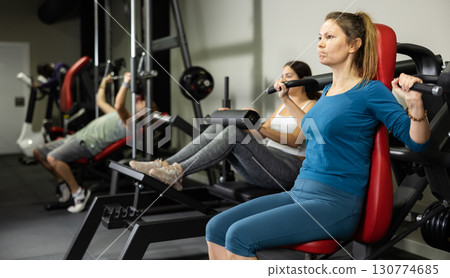 Young female training trains muscles of arms and press on simulator in gym Young female training trains muscles of arms and press on simulator in gym 130774685