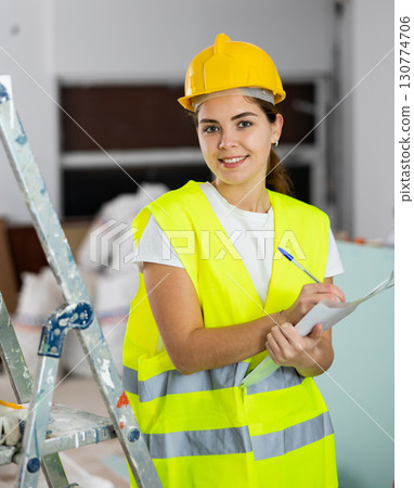 Positive female civil engineer taking notes while checking construction site Positive female civil engineer taking notes while checking construction site 130774706