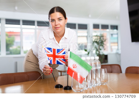 Positive young woman putting little flag of Great Britain on table next to the flag of Iran 130774709