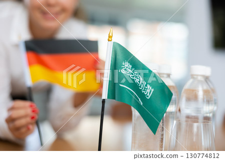 Preparing for business negotiations - woman sets small flags of countries of Saudi Arabia and Germany on table 130774812