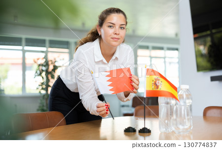 Young woman putting Bahrain and Spain flags on table in office Young woman putting Bahrain and Spain flags on table in office 130774837
