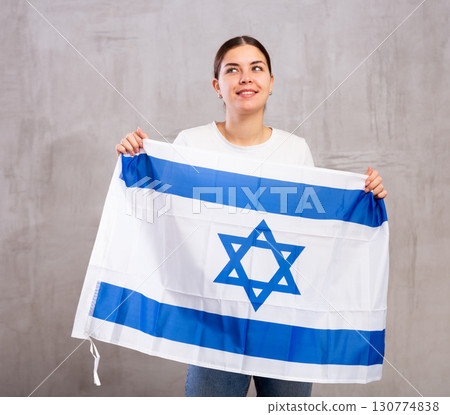 Joyous young woman holding Israel flag against unicoloured background 130774838