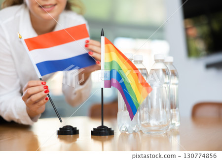 Young woman putting Netherlands and LGBT flags on table in office Young woman putting Netherlands and LGBT flags on table in office 130774856