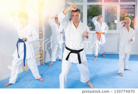 Middle-aged trainer practicing kata standing in row with preteen attendees of karate classes 130774870