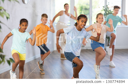 African boy dances vogue in choreographic school, friends and teacher dance in gym blurry background African boy dances vogue in choreographic school, friends and teacher dance in gym blurry background 130774894