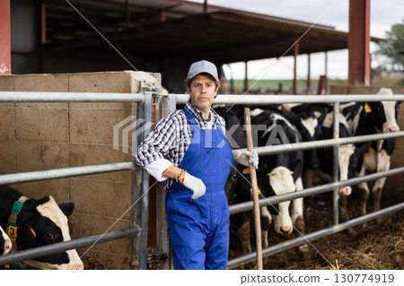 Adult male farmer posing while feeding cows at farm 130774919