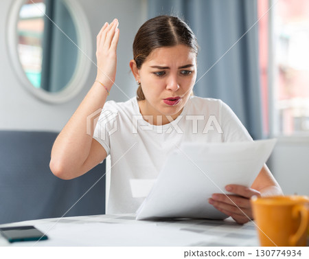 Upset woman with financial documents sitting at the table Upset woman with financial documents sitting at the table 130774934