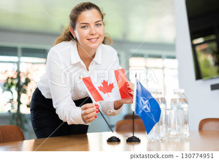 Female secretary places flags of the NATO (OTAN) and Canada on the table before negotiations of top political figures Female secretary places flags of the NATO (OTAN) and Canada on the table before negotiations of top political figures 130774951