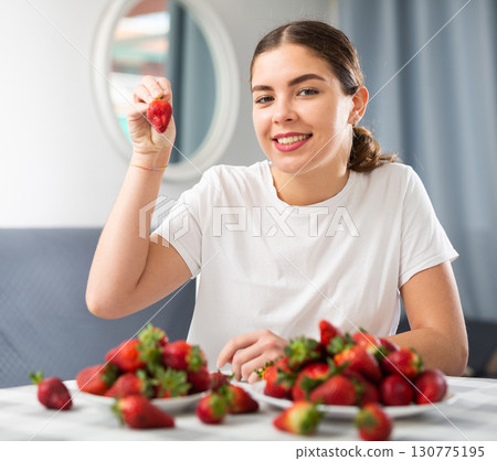 Young woman eating strawberry at home 130775195