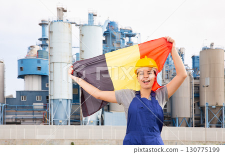 Happy young woman worker with flag of Belgium against background of factory Happy young woman worker with flag of Belgium against background of factory 130775199