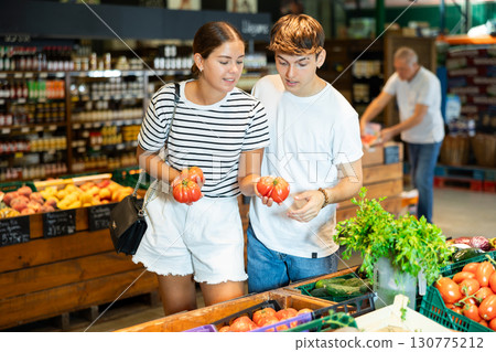 Young woman and young guy choose tomatoes in grocery store 130775212