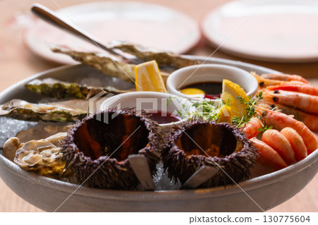 Seafood (oysters, shrimps, sea-urchins, mussels) are decoratively put on ice in a big plate Seafood (oysters, shrimps, sea-urchins, mussels) are decoratively put on ice in a big plate 130775604