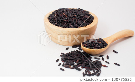 Riceberry rice grains in a wooden bowl and spoon with scattered seeds on a clean white background, representing healthy food and organic nutrition. Riceberry rice grains in a wooden bowl and spoon with scattered seeds on a clean white background, representing healthy food and organic nutrition. 130775825