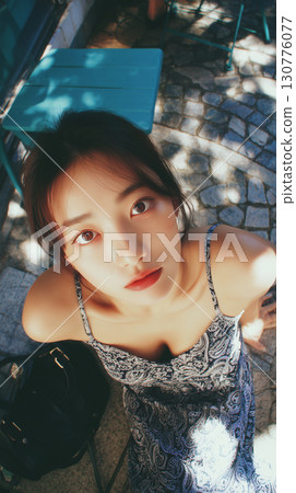 Young woman enjoying a sunny day outdoors in a patterned dress at a charming location with delightful shadows and light 130776077