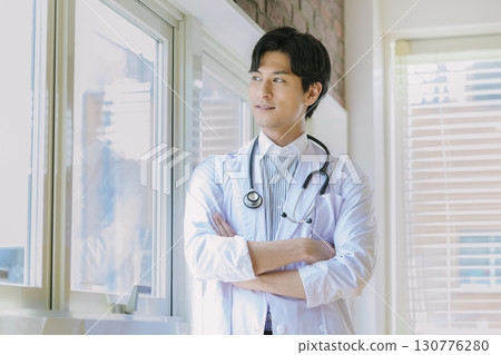 一位身穿白大褂的年輕醫生站在窗邊 130776280