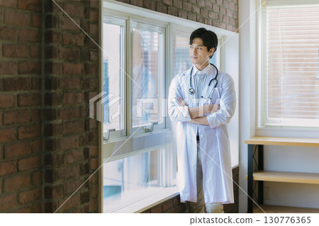 A young doctor in a white coat standing by the window 130776365