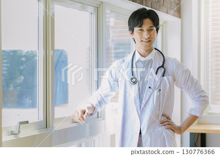 A young doctor in a white coat standing by the window 130776366