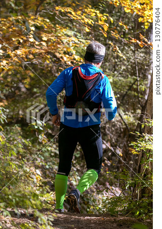 Rear view male athlete with camelback running autumn trail race 130776404