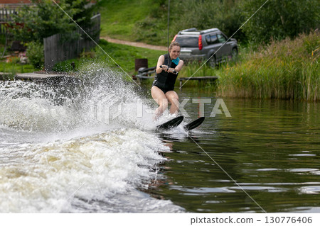 Woman amateur on water ski crosses wave with splashing water Woman amateur on water ski crosses wave with splashing water 130776406