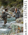 Friendship and Mutual Aid: Two Happy Friends On A Hiking Trip Hand-In-Hand, Showing Trust And Care In A Natural Setting. 130776471