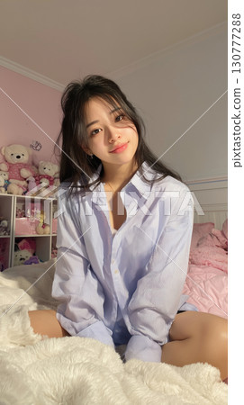 Portrait of a young woman indoors, dressed casually and smiling in a cozy room decorated with soft colors and plush toys 130777288