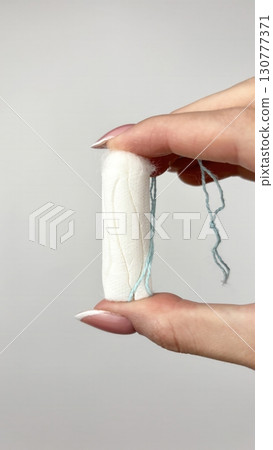 Female hand holding white tampon on clean white background, close up. Feminine hygiene product for menstruation, womens health and period care concept 130777371