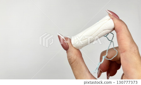 Female hand holding white tampon on clean white background, close up. Feminine hygiene product for menstruation, womens health and period care concept Female hand holding white tampon on clean white background, close up. Feminine hygiene product for menstruation, womens health and period care concept 130777373