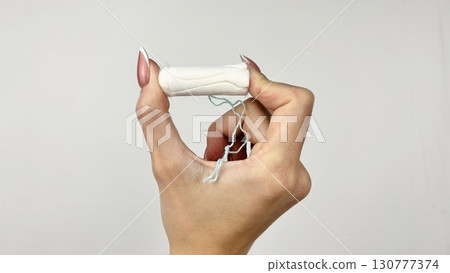 Female hand holding white tampon on clean white background, close up. Feminine hygiene product for menstruation, womens health and period care concept Female hand holding white tampon on clean white background, close up. Feminine hygiene product for menstruation, womens health and period care concept 130777374