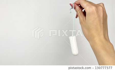 Female hand holding white tampon on clean white background, close up. Feminine hygiene product for menstruation, womens health and period care concept Female hand holding white tampon on clean white background, close up. Feminine hygiene product for menstruation, womens health and period care concept 130777377