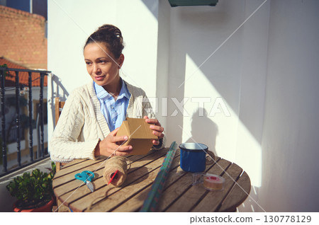Woman Wrapping Gift Box Outdoors on Sunny Day with Craft Supplies 130778129