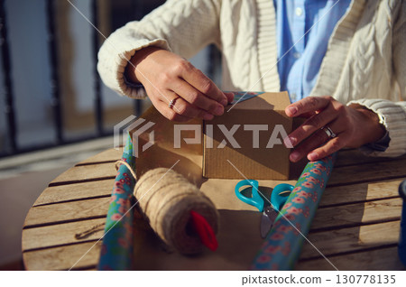 Close-Up of Wrapping a Gift with Decorative Paper and Supplies Outdoors Close-Up of Wrapping a Gift with Decorative Paper and Supplies Outdoors 130778135