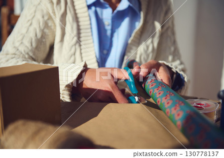 Hands Wrapping Gift with Decorative Paper and Scissors 130778137