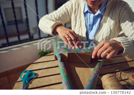 Woman Wrapping a Gift Outdoors with Floral Paper 130778142