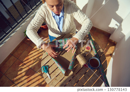 Woman Wrapping a Gift on a Sunny Terrace Table Woman Wrapping a Gift on a Sunny Terrace Table 130778143