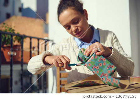 Woman Wrapping a Floral Gift on a Sunny Outdoor Balcony 130778153